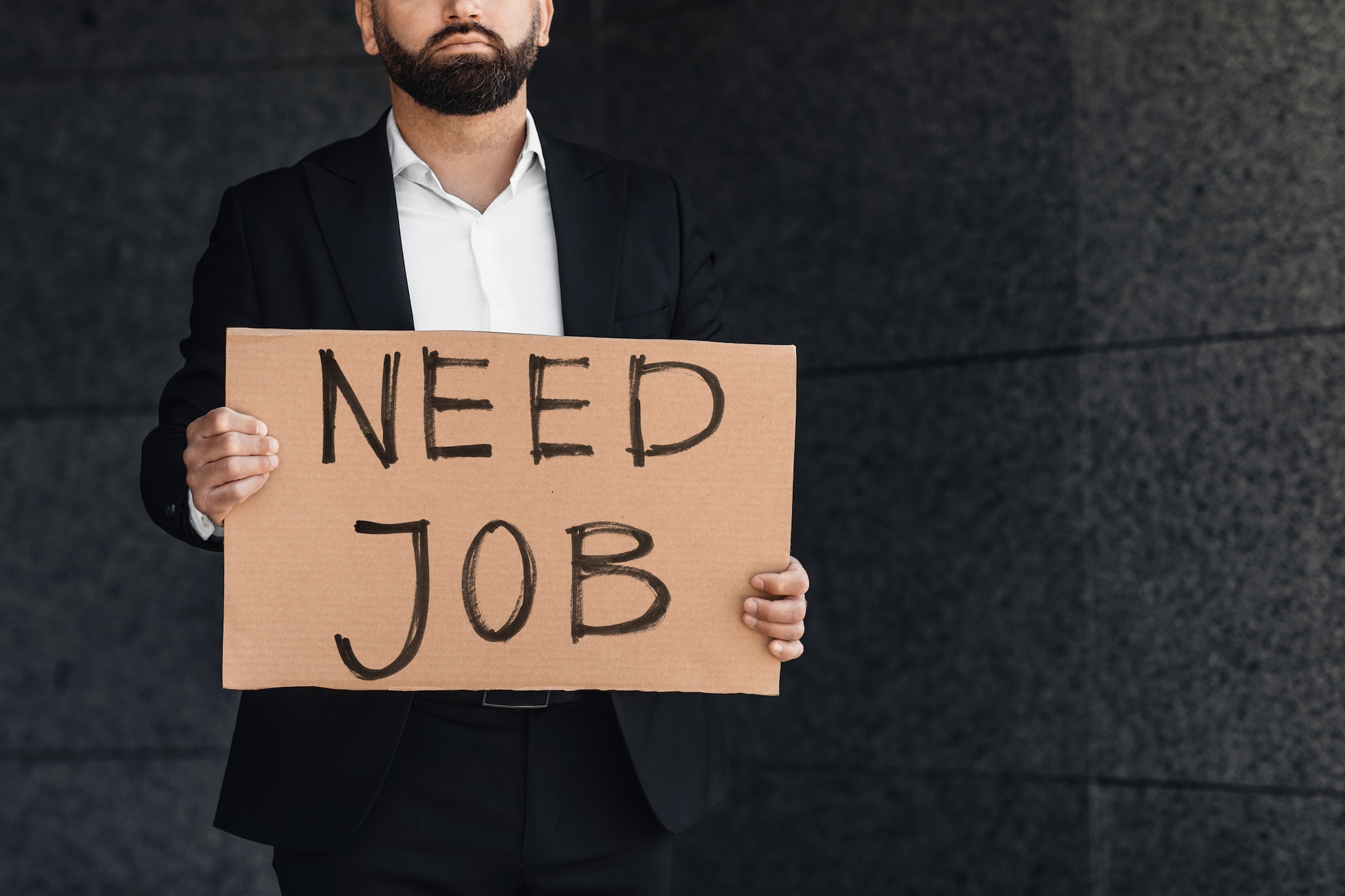 Despaired businessman lost work holding need job cardboard placard outside, standing near business