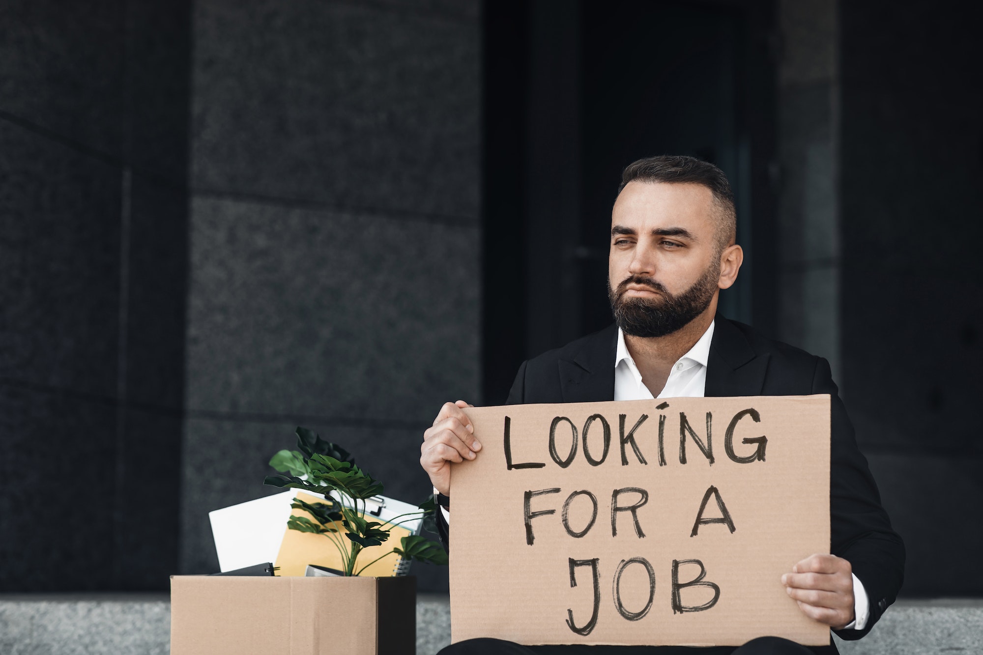 Unhappy unemployed man holding cardboard sign with Looking For a Job written text