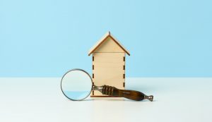 Magnifier and wooden house on a blue background. Real estate rental
