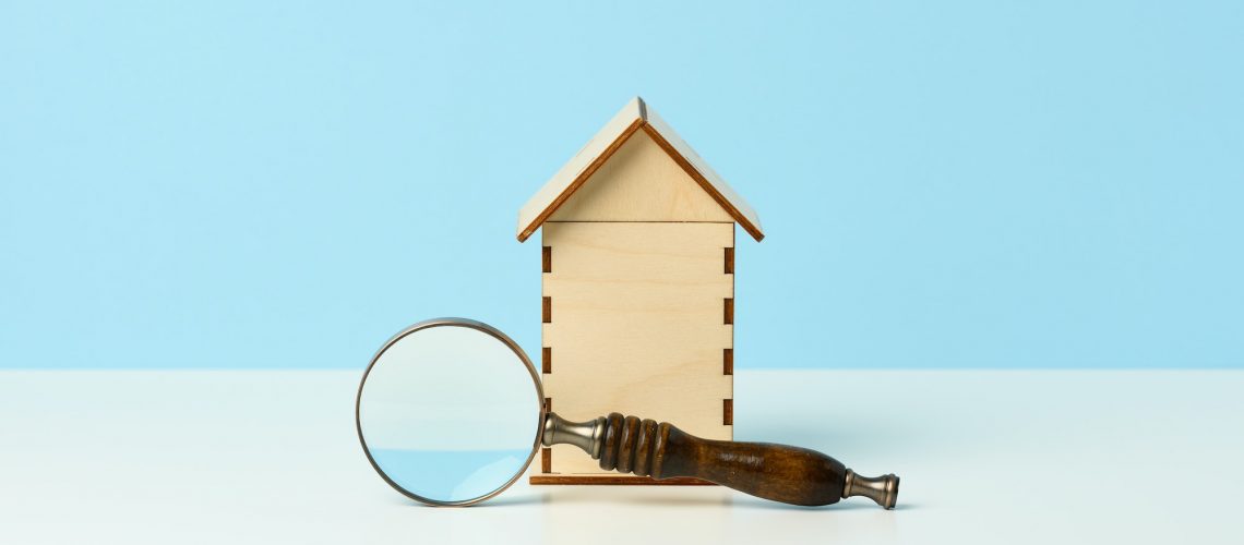 Magnifier and wooden house on a blue background. Real estate rental